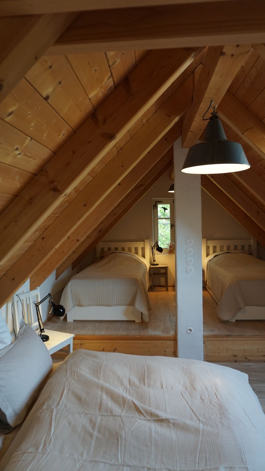 Schlafzimmer im Dachgeschoss mit Holzbalken und drei Betten mit weißer Bettwäsche.