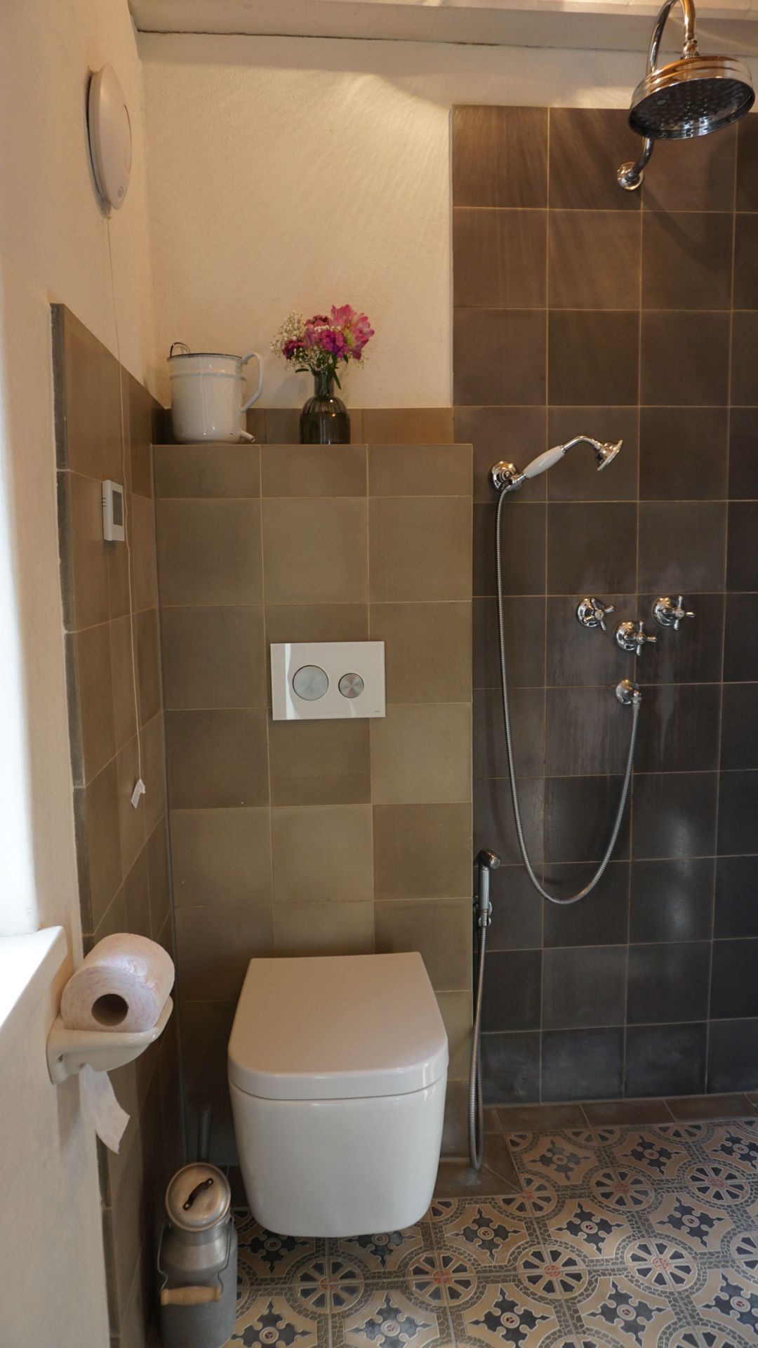 Badezimmer mit gefliester Dusche, Toilette und gemustertem Boden. 