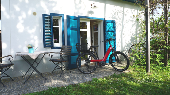 Weißes Gebäude mit blauen Fensterläden und einem davor geparkten roten Fahrrad.