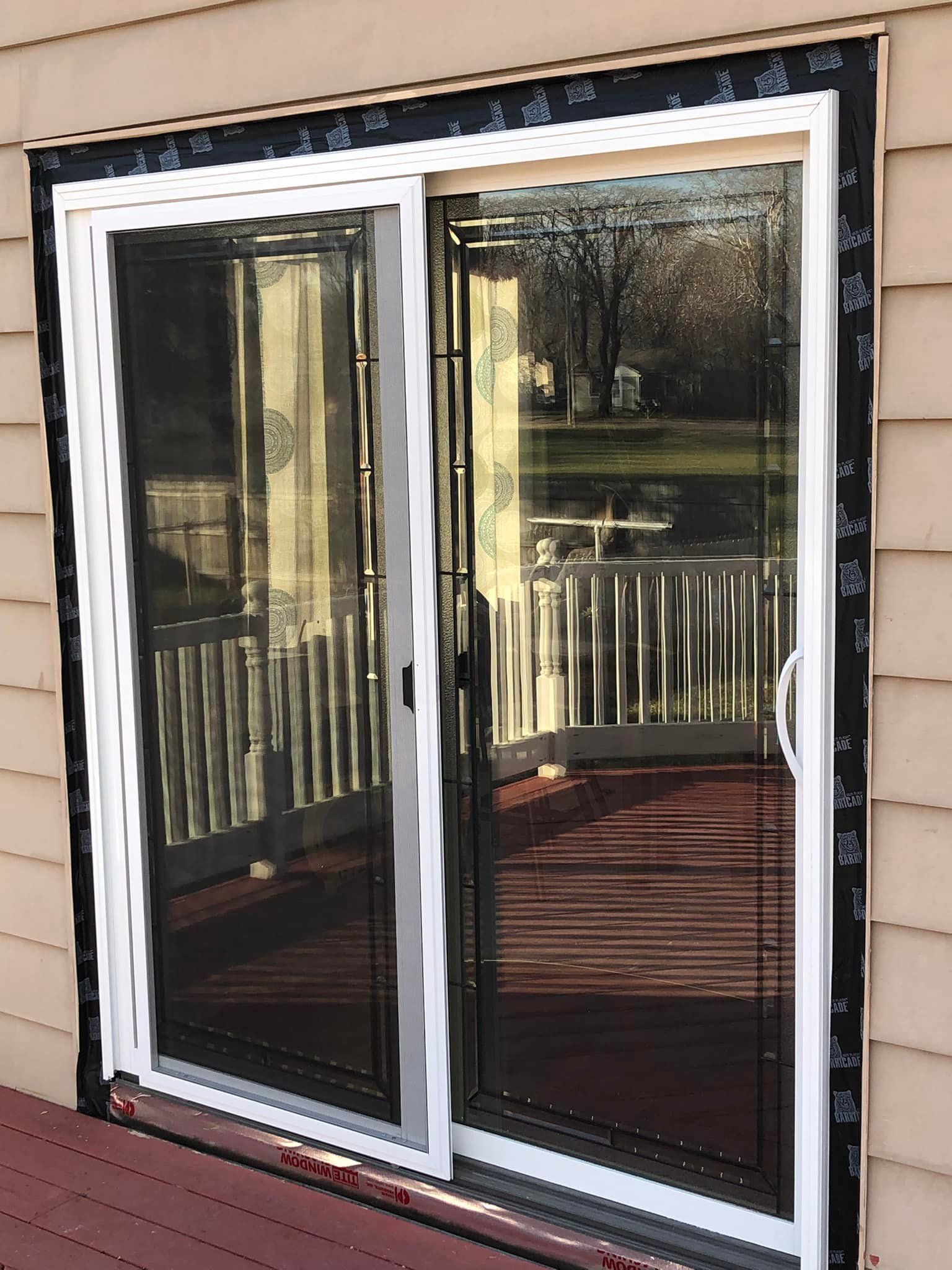 Sliding glass door with a screen, white frame, on a deck, tan siding, black flashing.