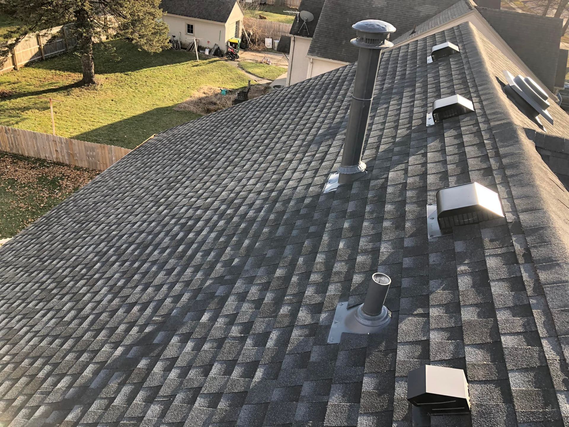 A gray asphalt shingle roof with vents and a chimney; a sunny outdoor setting.