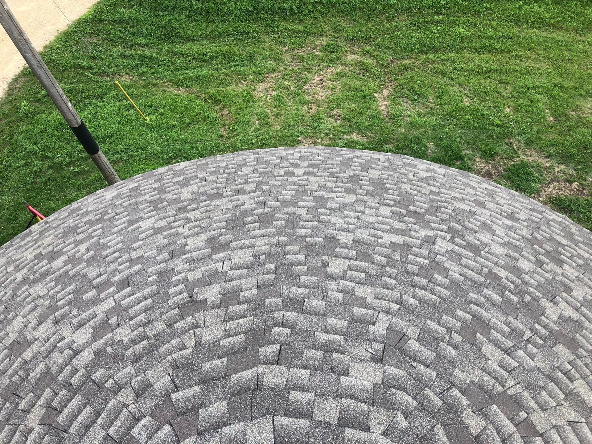 Overhead view of a gray shingled dome roof with green grass in the background.