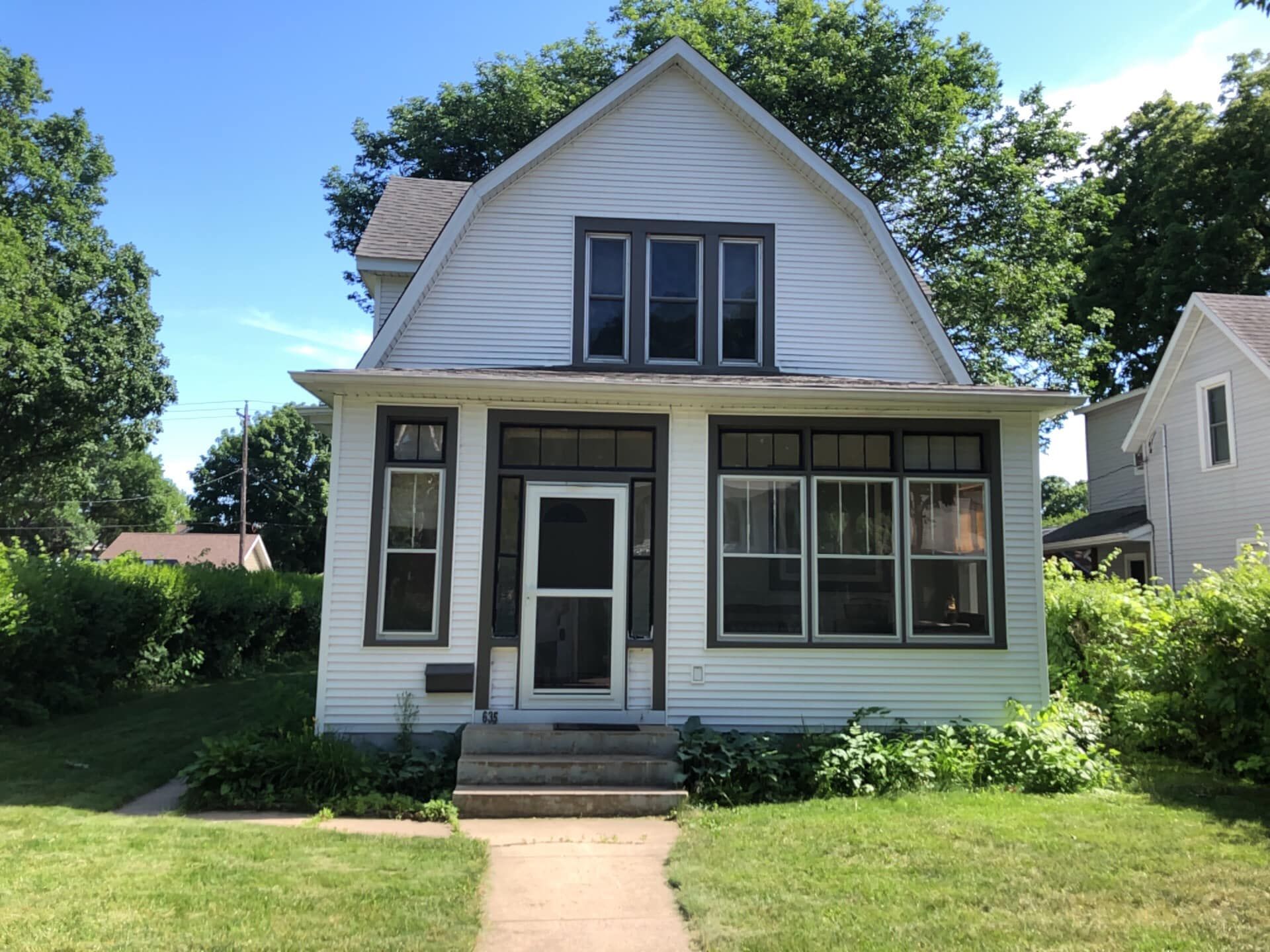 White house with dark trim, front door, windows, and a green lawn.