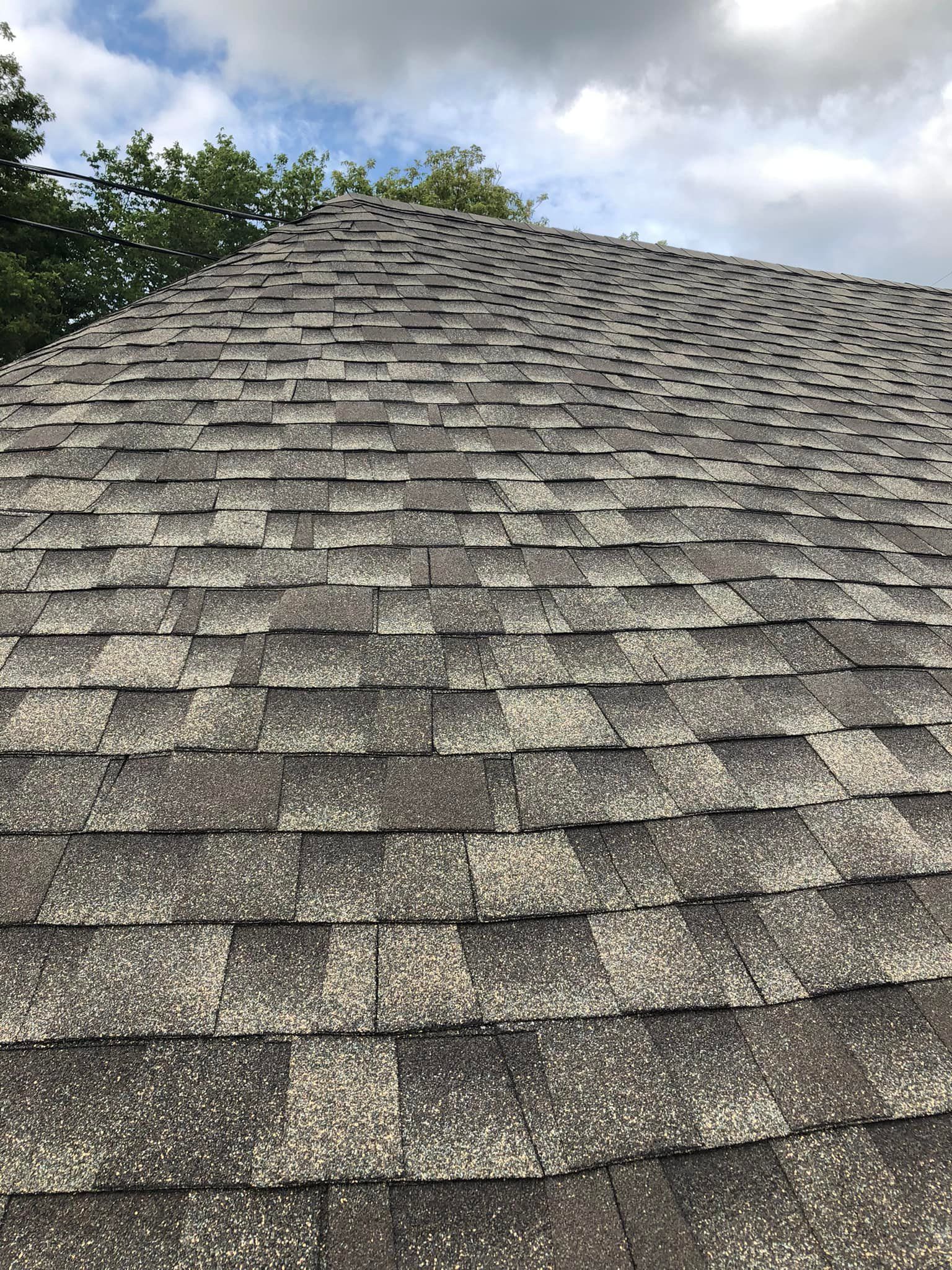 Close-up of an aged asphalt shingle roof under a cloudy sky.
