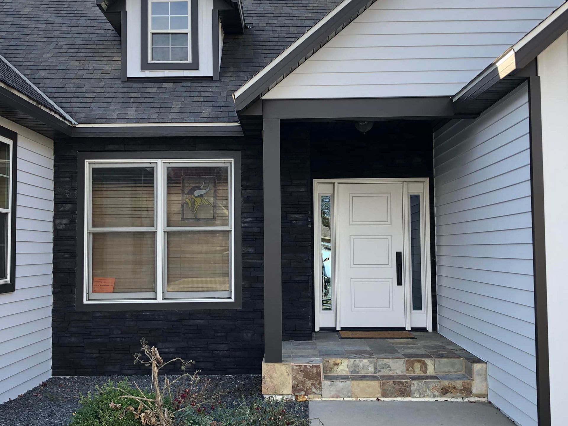 Black and gray house exterior with white door under a porch.