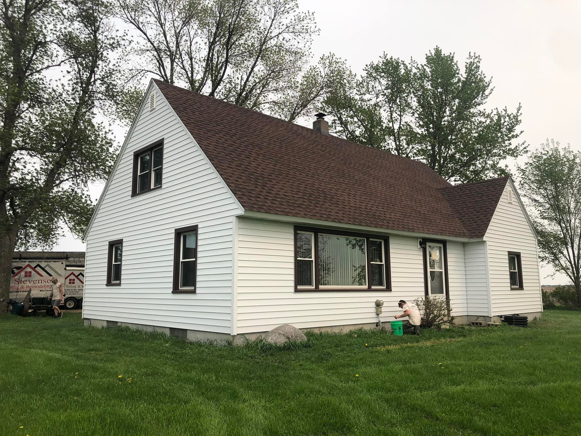 White house with brown roof and black window frames on a grassy lawn.