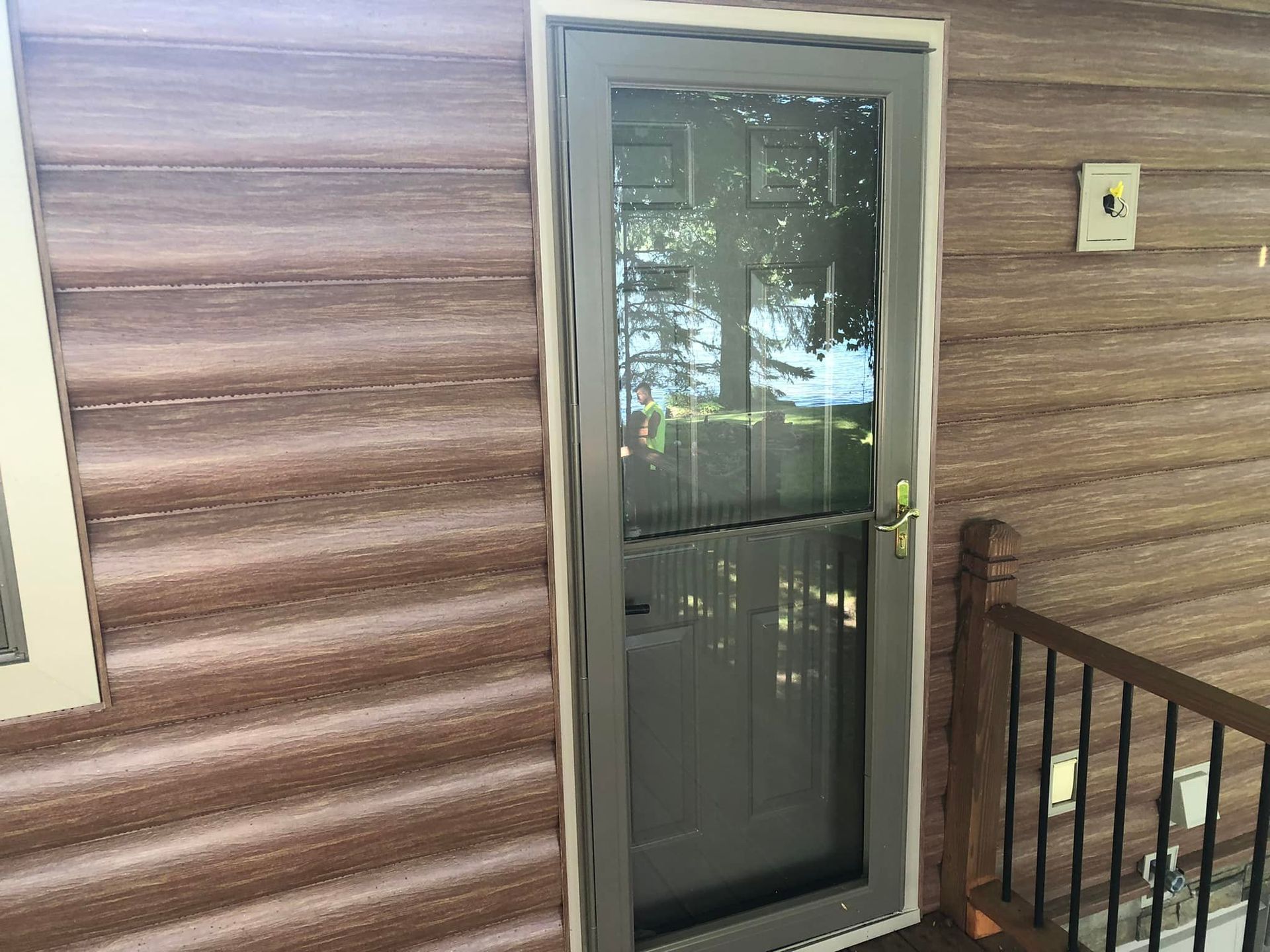 Grey screen door on a brown house with a small porch and black railing.