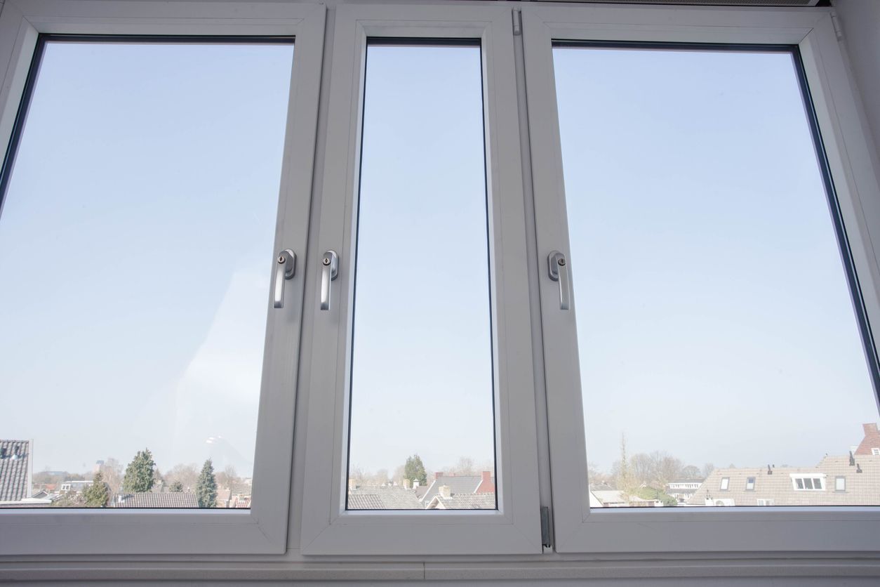 White framed triple window overlooking a blue sky and rooftops.