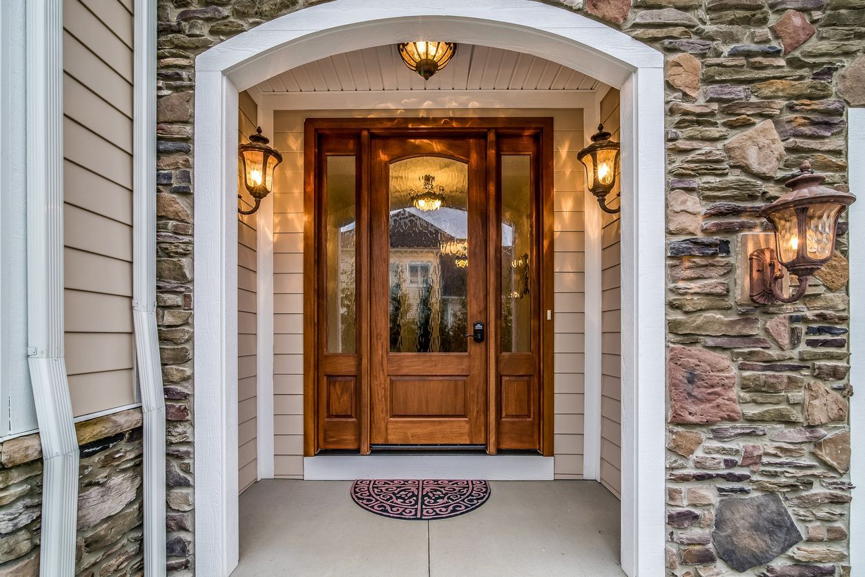 Wooden front door with sidelights under a stone archway, flanked by sconces.