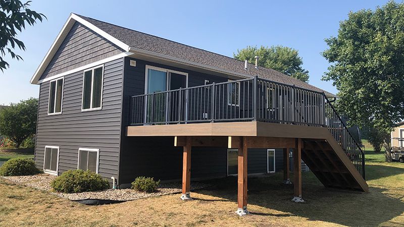 Dark grey house with a brown deck, metal railing, and wooden stairs.