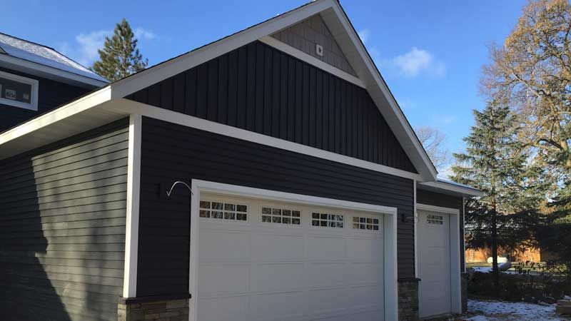 A dark gray garage with white trim and doors, against a blue sky.