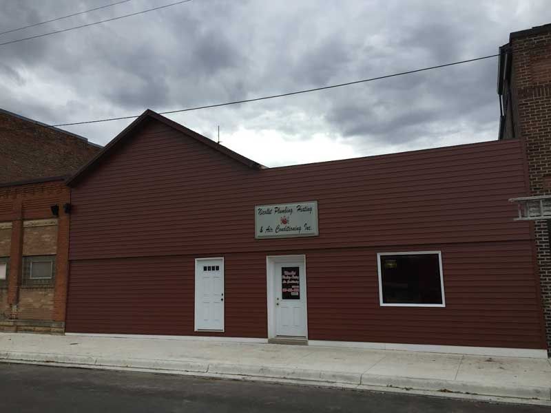A brown building with a sign, two white doors, and a window under a cloudy sky.