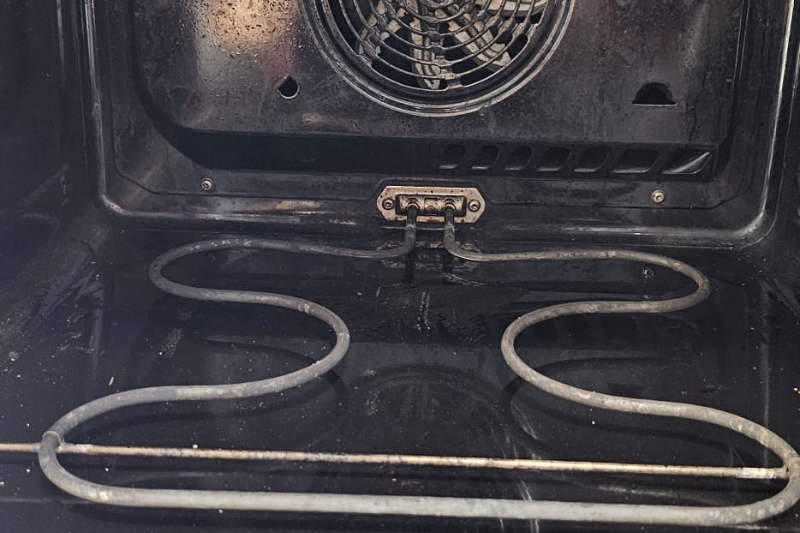 Schmutziger Ofeninnenraum mit sichtbarem Heizelement und Ventilator.