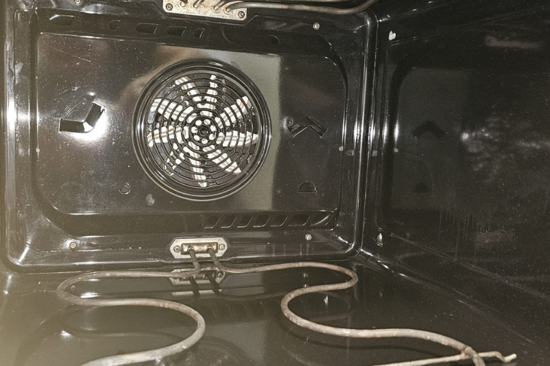 Innenansicht eines schwarzen Ofens mit Ventilator auf der Rückseite und Heizelement unten.