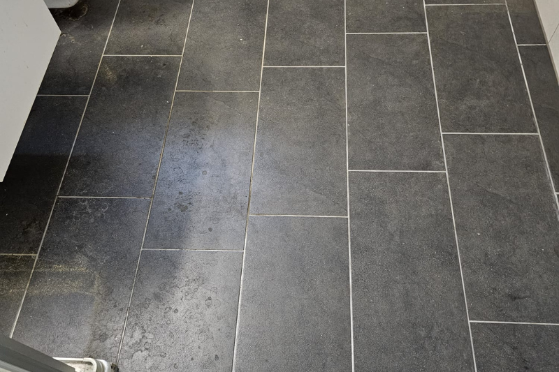 Dunkelgrauer rechteckiger Fliesenboden mit hellen Fugenlinien.