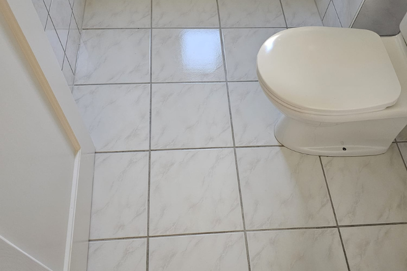 Weiß gefliester Badezimmerboden mit weißer Toilette.