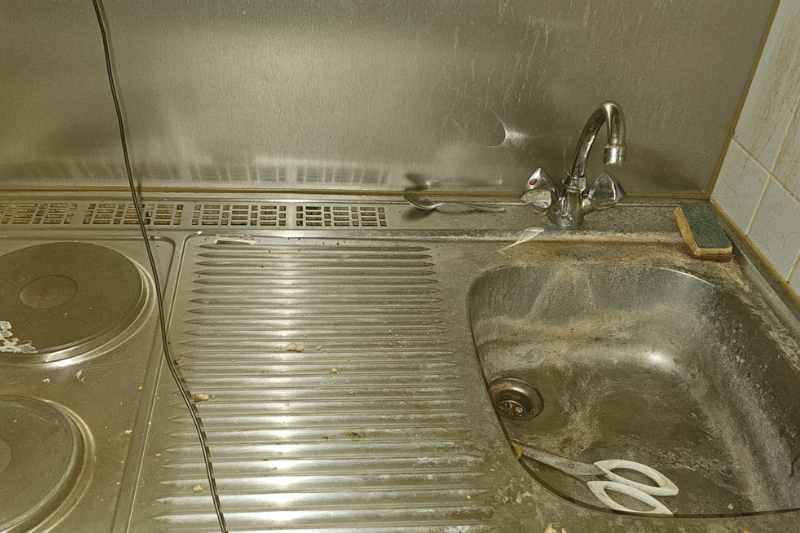 Schmutzige Küchenspüle und Herd mit Metalloberflächen und einem Schwamm, die Abnutzungserscheinungen aufweisen.