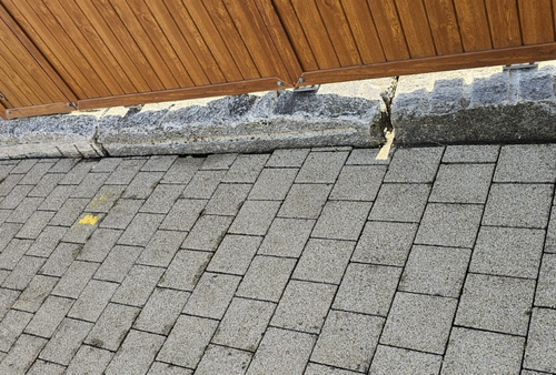 Graue Asphaltschindeln, eine abgebrochene Betonkante und Holzverkleidungen von einem Dach.