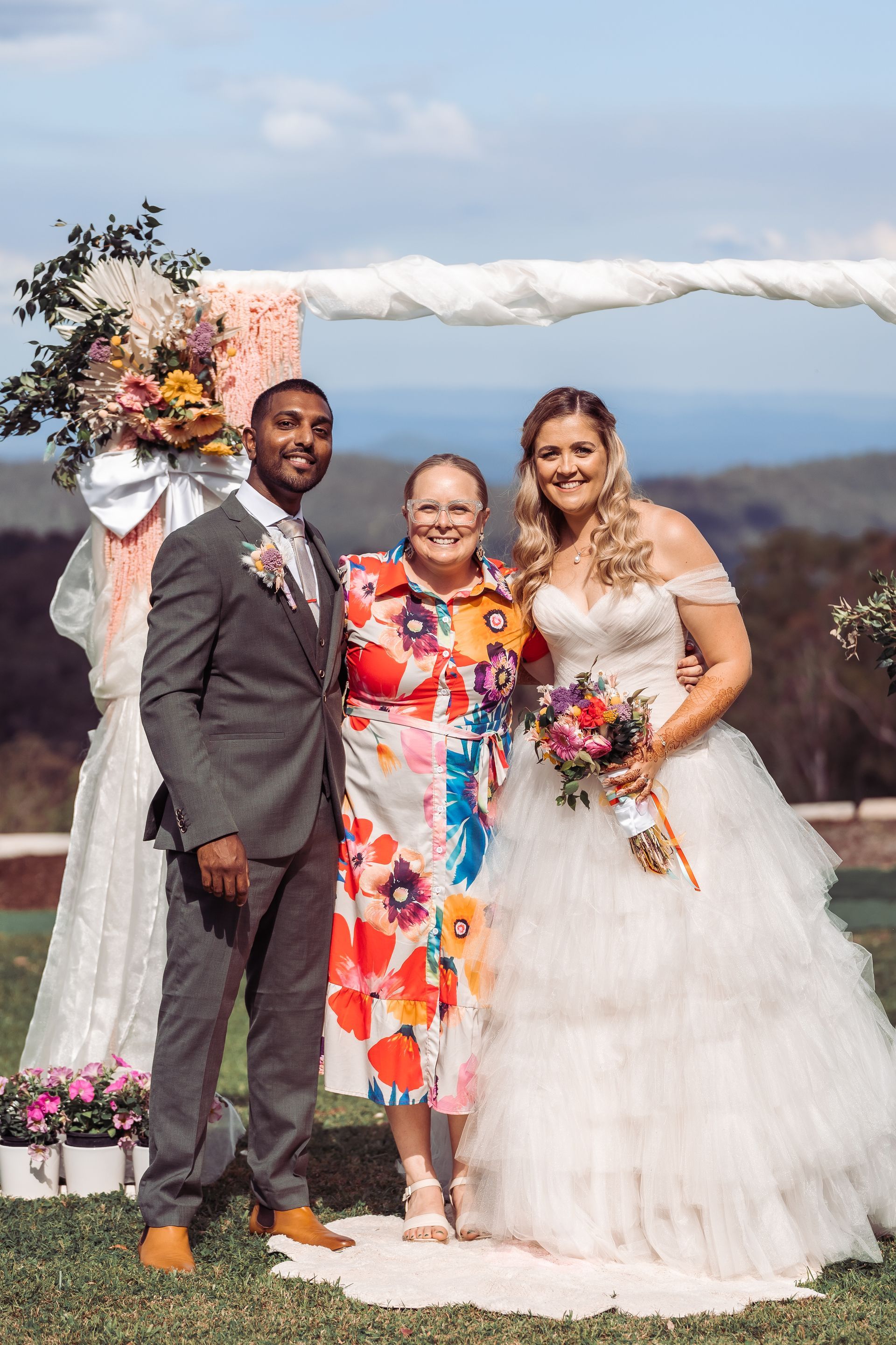 Couple poses with officiant outdoors after wedding ceremony, with floral arch.