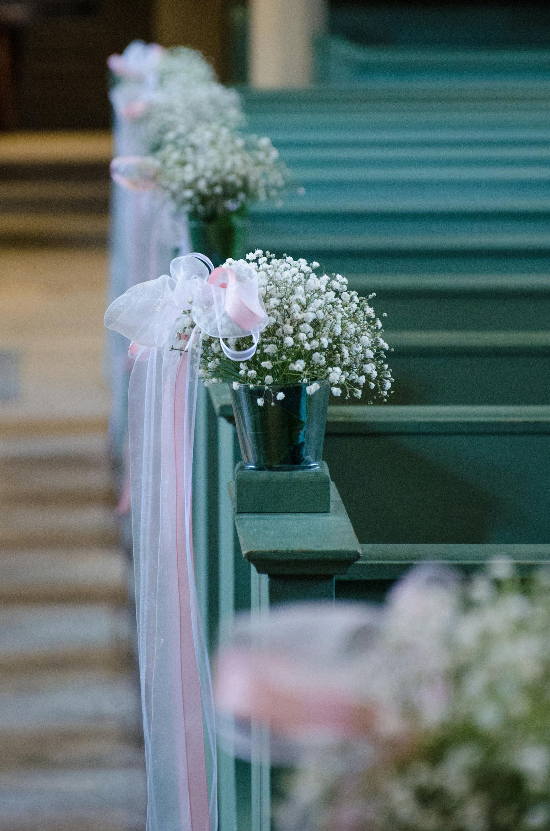 Baby's breath flowers in vases, decorated with pink ribbons, line church pews.