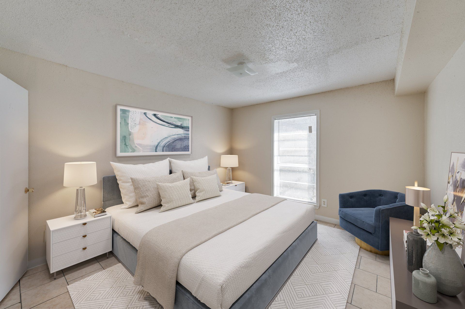 Well-appointed bedroom in GIA Houston apartment, featuring a large bed, abstract artwork, and a stylish blue accent chair.