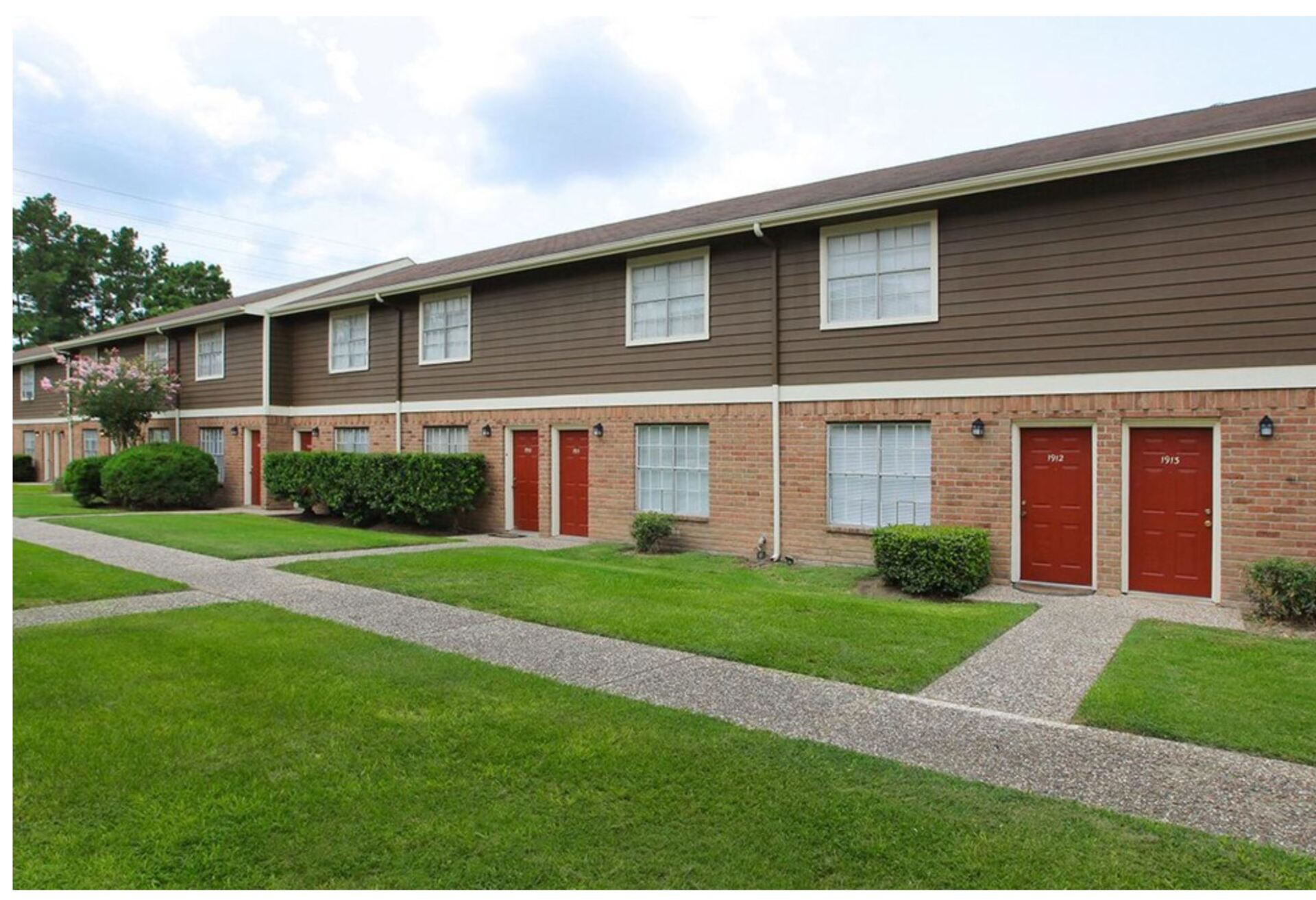 Exterior of two-story Gia Spring Branch apartment building with red doors & landscaped grounds in Houston.