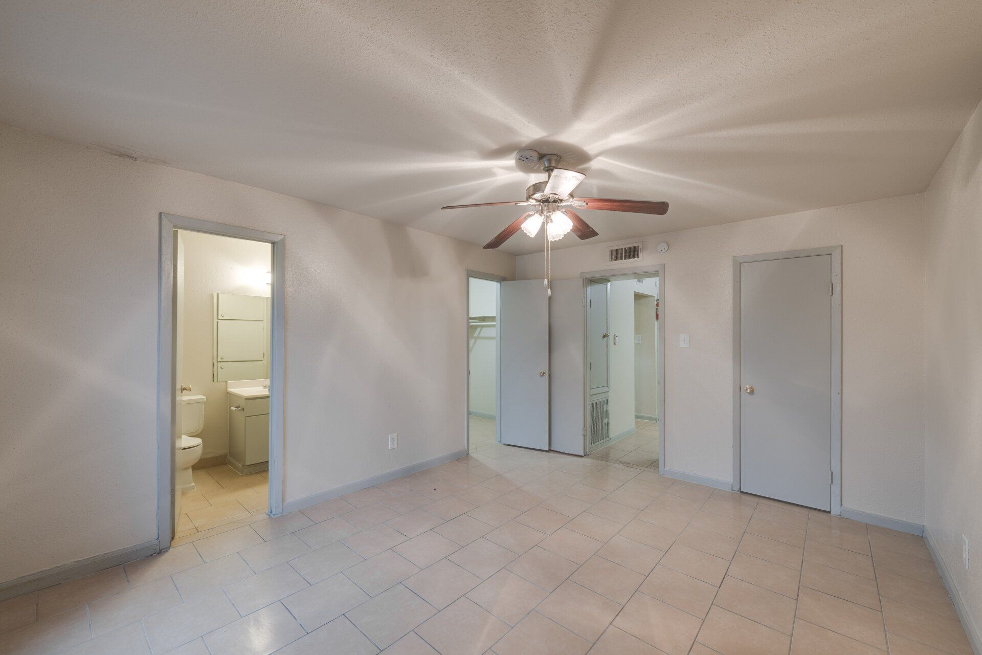 Spacious bedroom area in Houston apartment for rent, with open floor plan, ensuite bath, tile flooring, and ceiling fan.