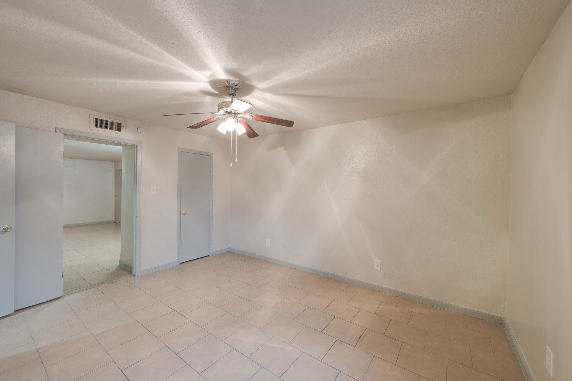 Spacious bedroom area in Houston apartment for rent, with open floor plan, ensuite bath, tile flooring, and ceiling fan.