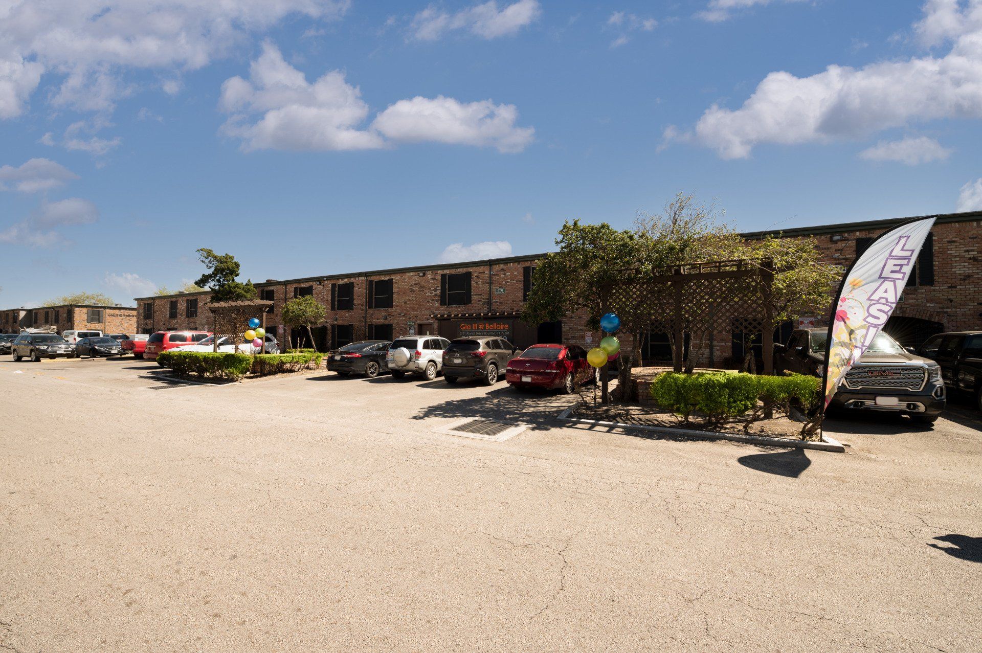 GIA Bellaire III Houston apartments parking lot with a LEASING Flag and brick partment building in the background.