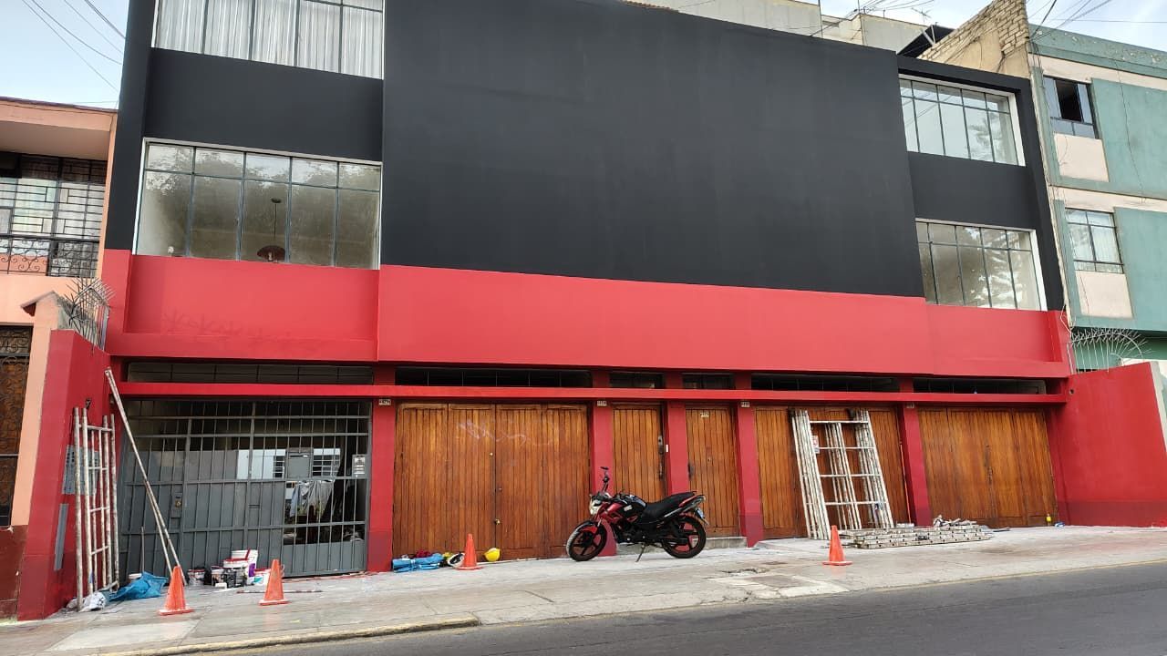 Exterior del edificio: Fachada roja y negra con puertas de madera y motocicleta estacionada en la acera.