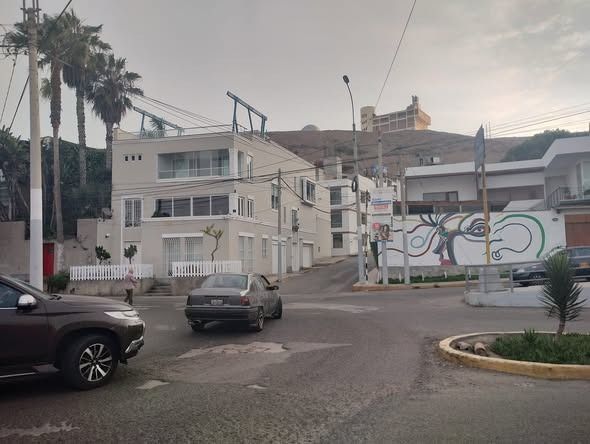 Escena callejera con edificios, palmeras y vehículos; cielo nublado.