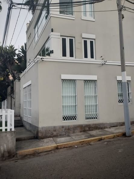 Edificio gris con molduras blancas y ventanas enrejadas, situado en una calle de la ciudad.