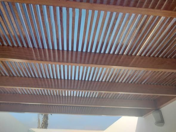 Techo de pérgola de lamas de madera, vigas marrones con cielo azul visible a través de los huecos.