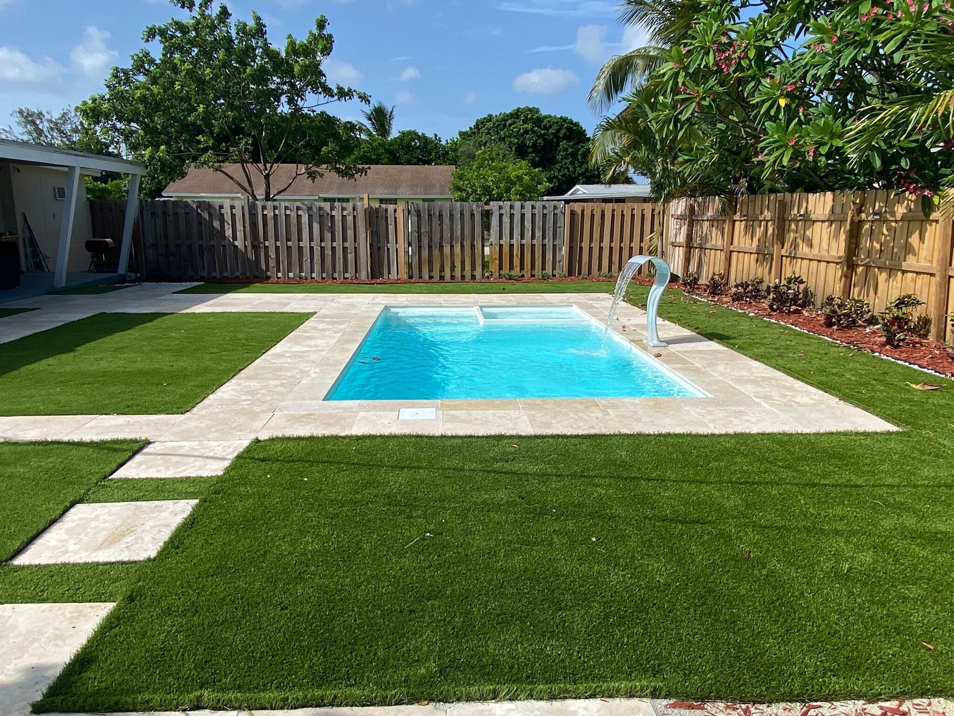 There is a swimming pool in the middle of a lush green backyard.