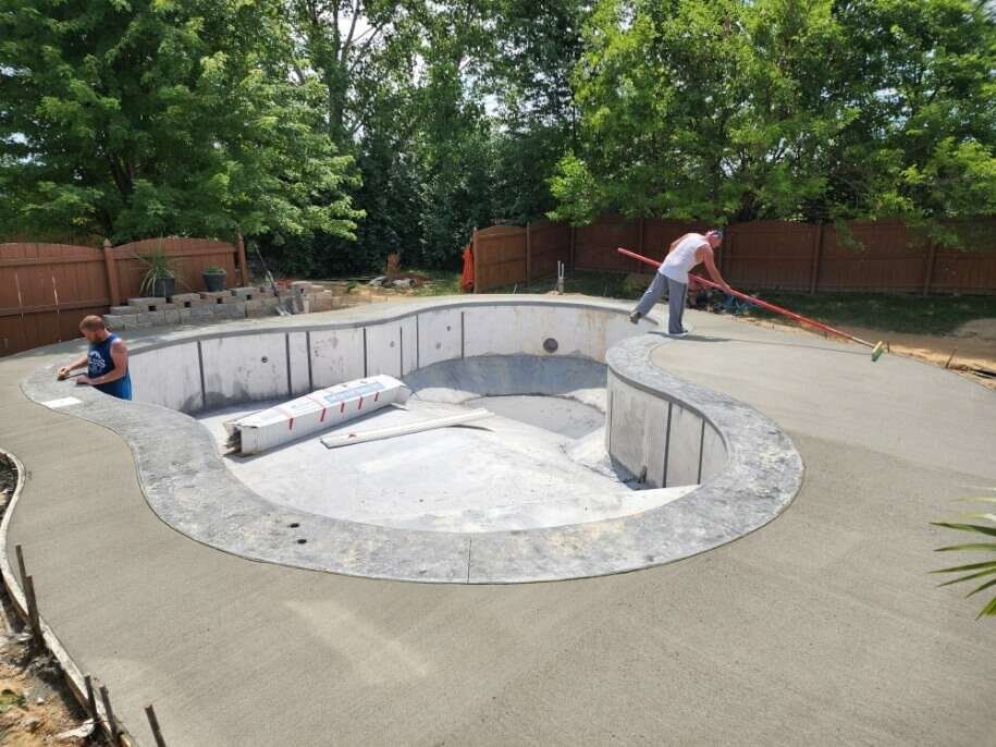 Two men are working on a concrete pool in a backyard.