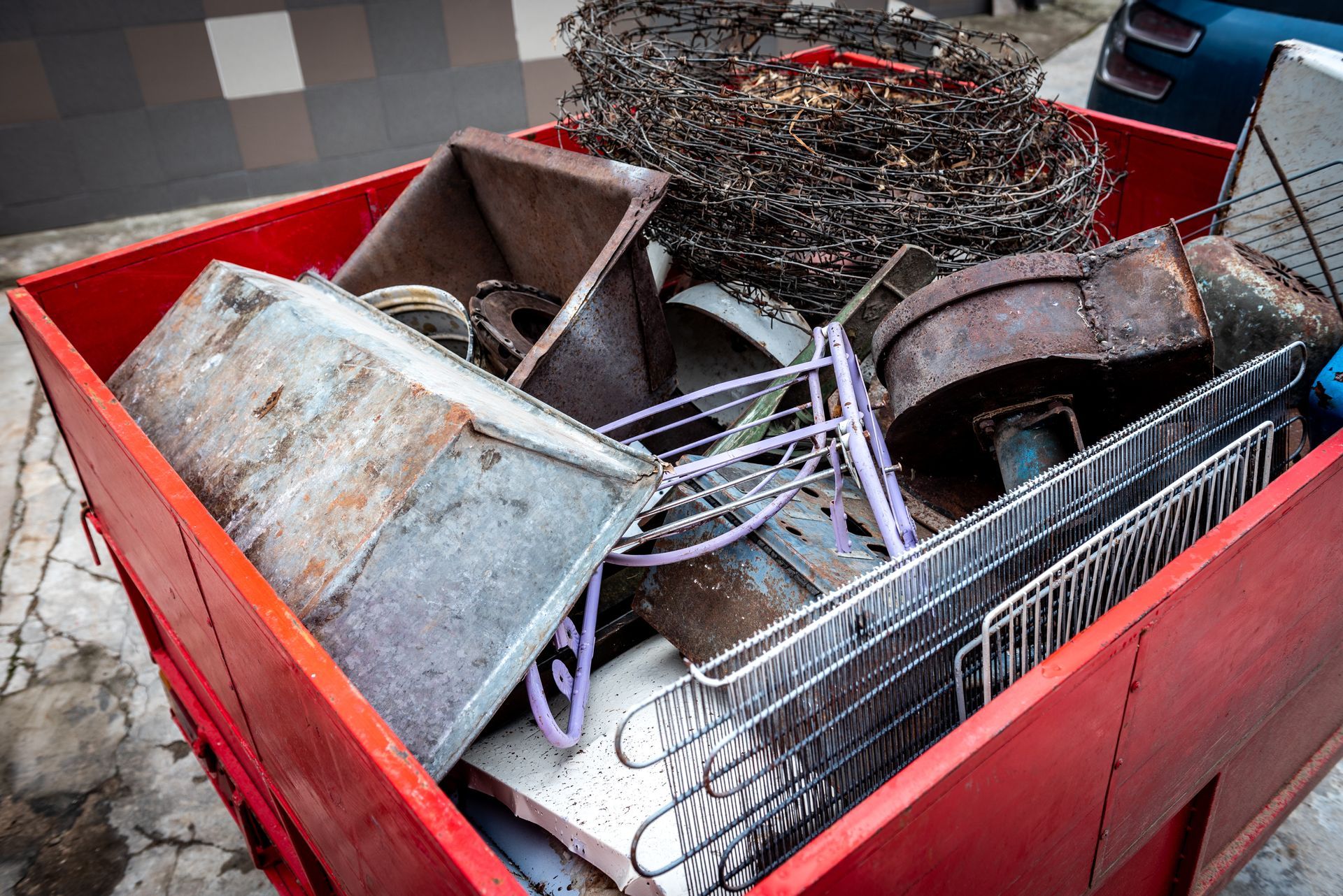 Red metal dumpster filled with assorted scrap metal items and wire.