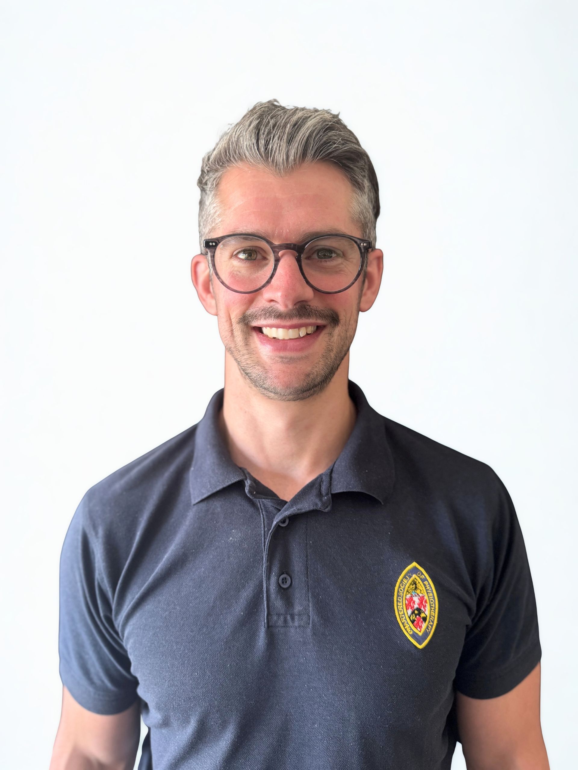 Man wearing glasses and navy polo shirt smiling in front of a white background.
