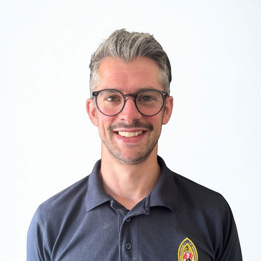 Man with graying hair, glasses, smiling in dark polo shirt, against white background.