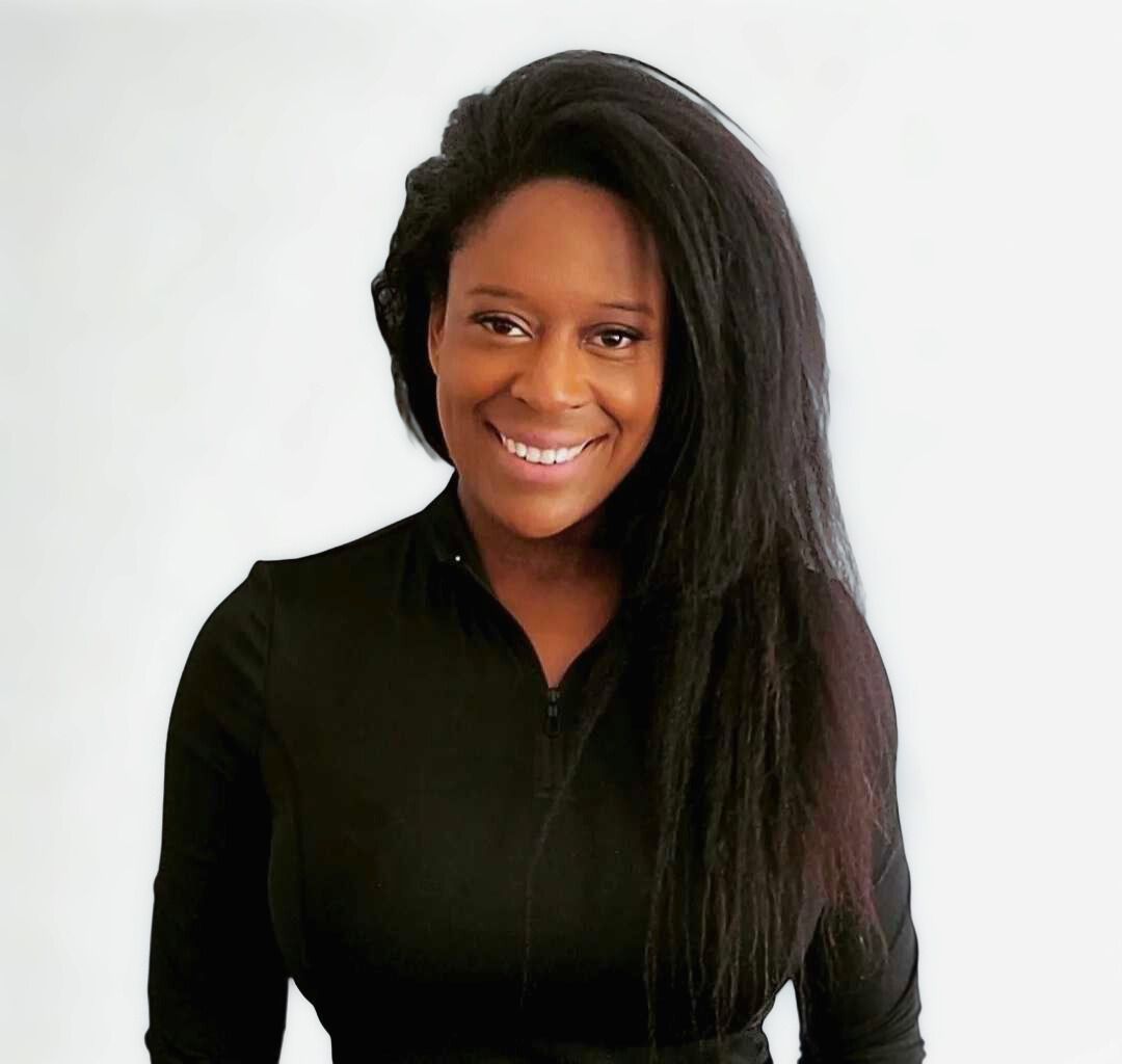 Woman with long, dark hair smiles; wears a black top, poses against a white backdrop.