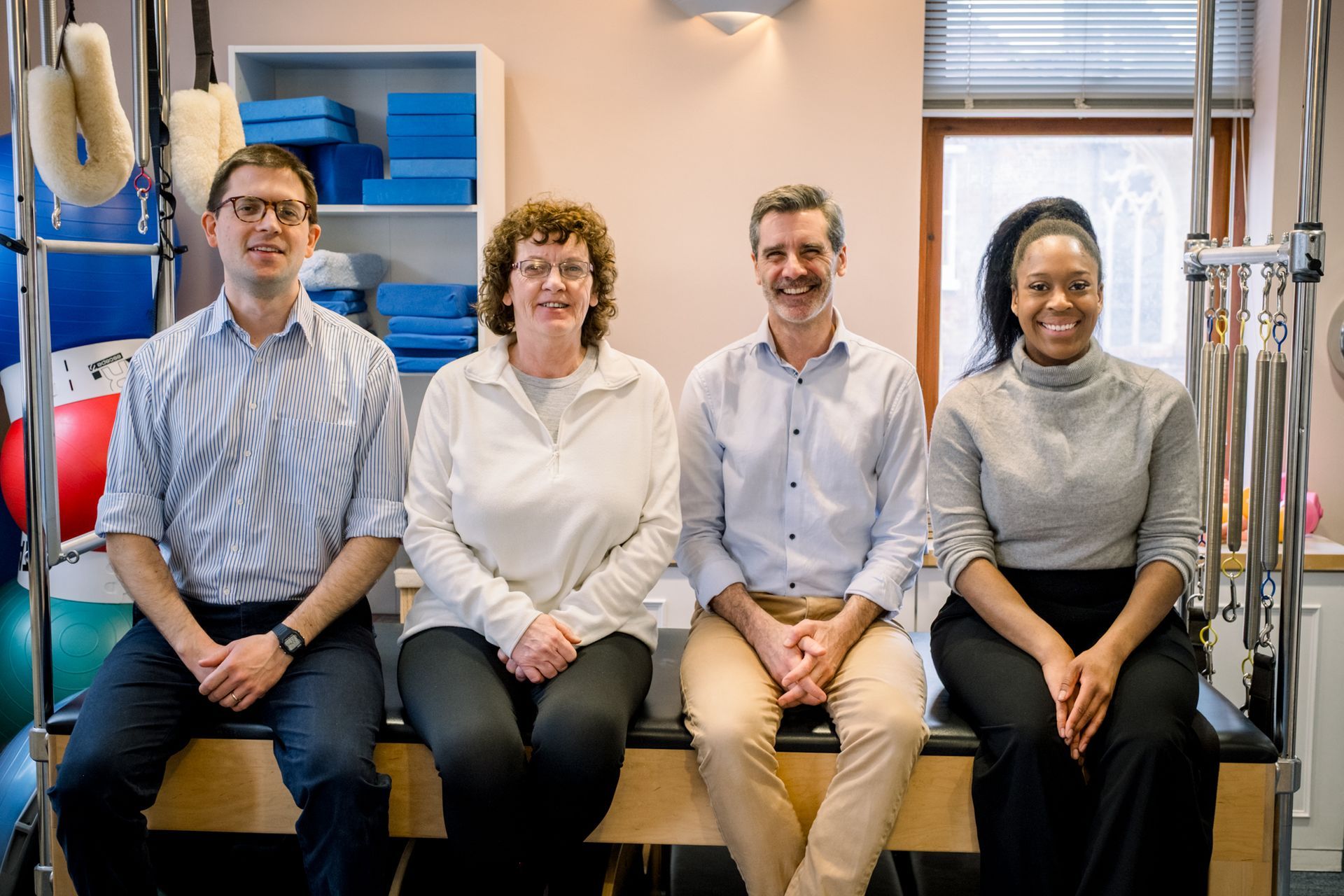 Four people seated together in a room with exercise equipment. They are smiling at the camera.