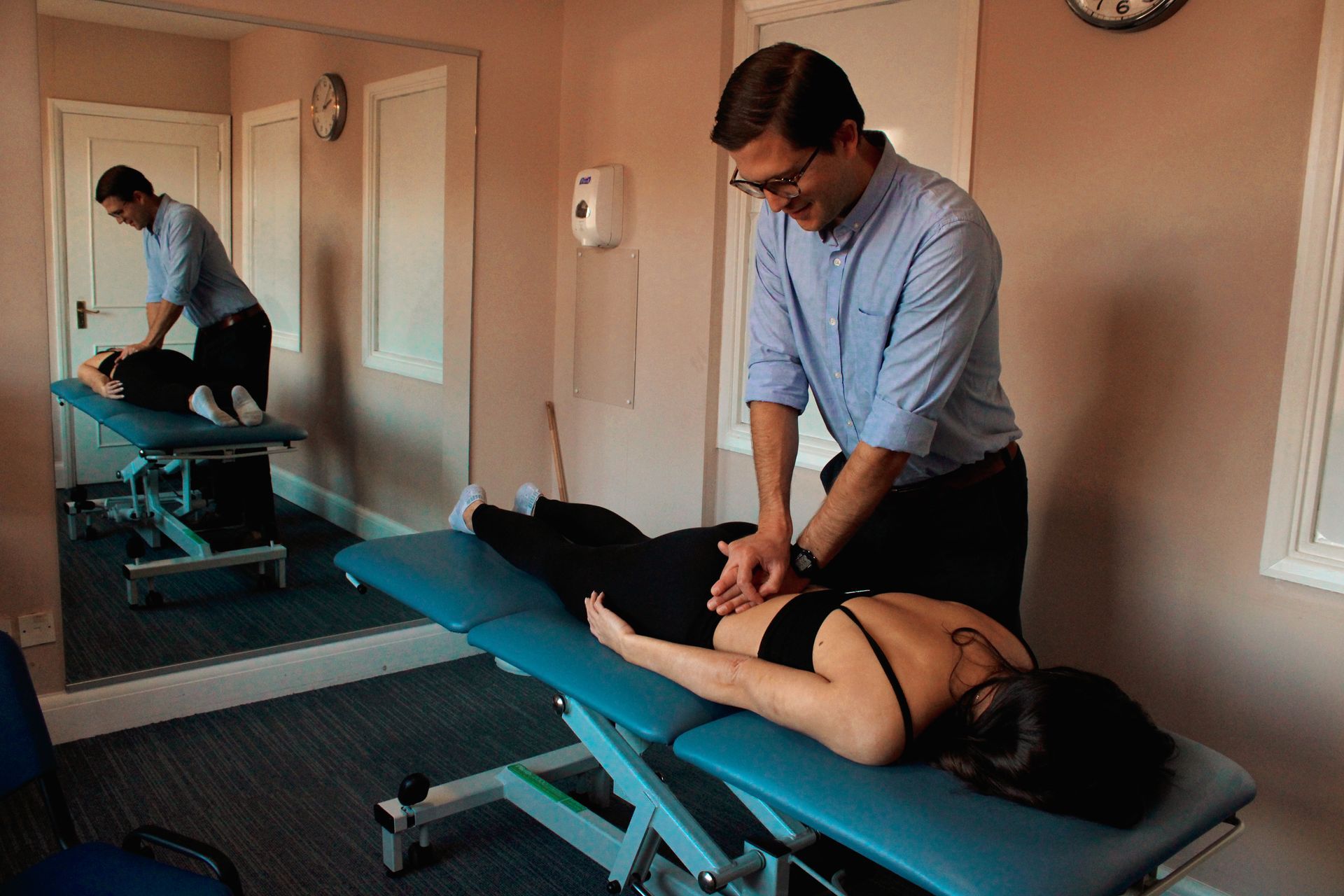 Therapist giving back treatment to a person lying on a teal table. Mirror shows therapist's reflection.