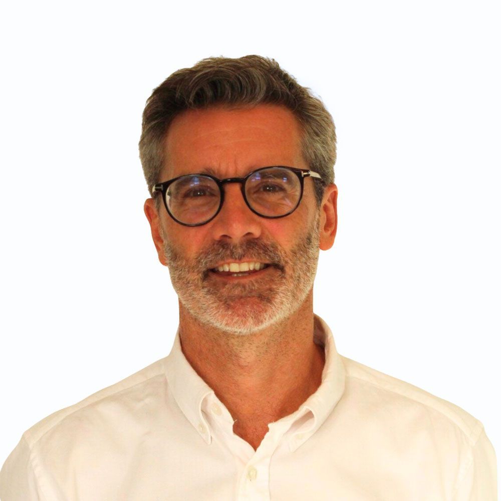 Man with glasses and grey beard smiles, wearing a white shirt.