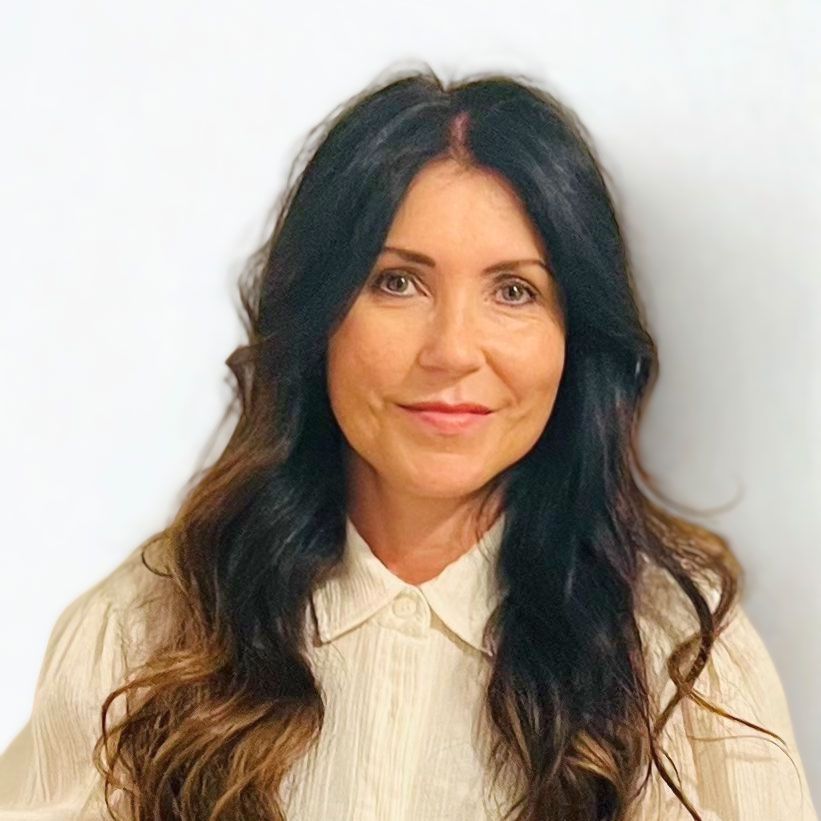 Woman with long, wavy brown hair, wearing a cream-colored collared shirt, smiling.