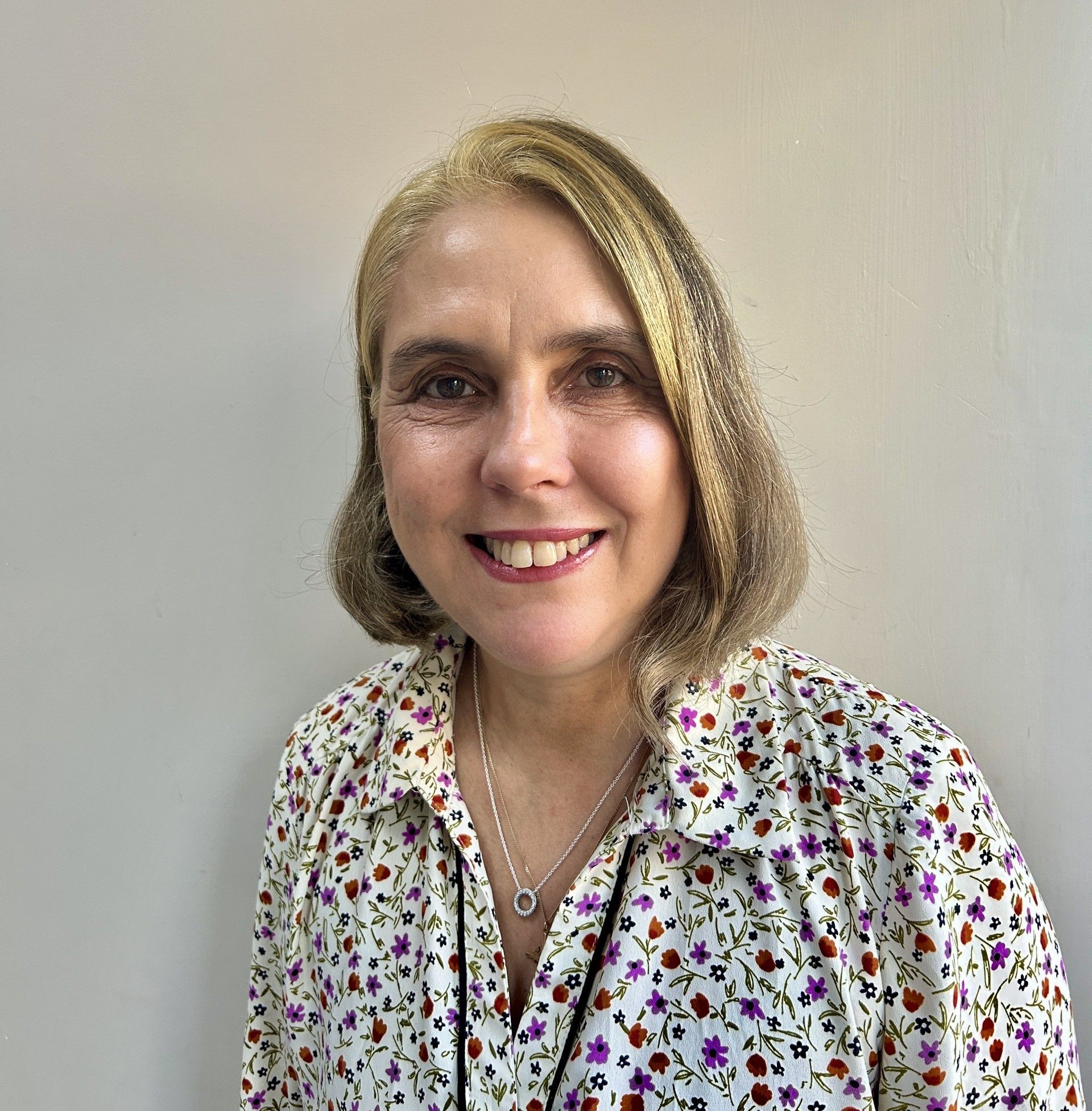 Woman with light brown hair and a floral shirt smiling at the camera.