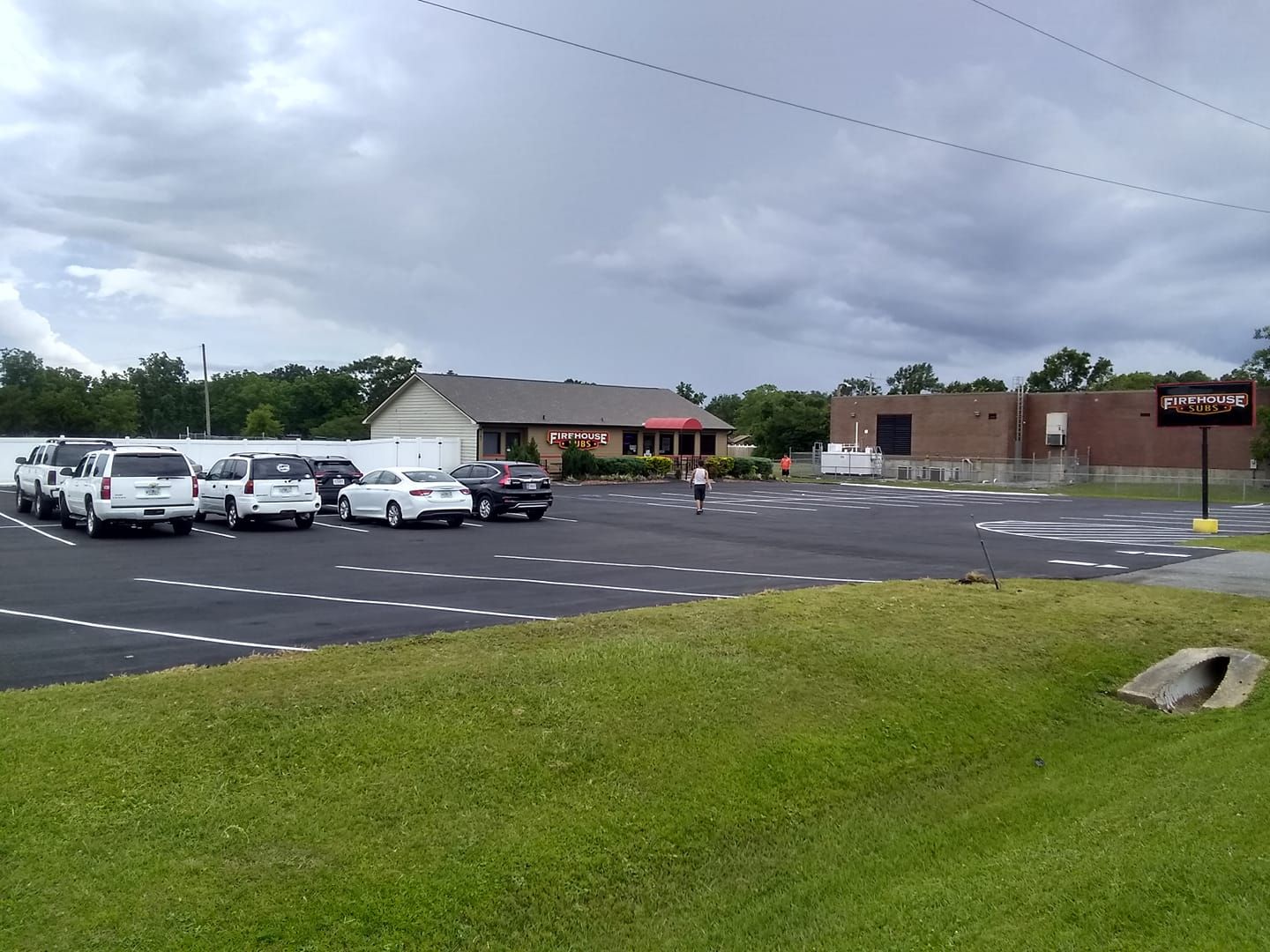 Parking lot with cars, a building with a red awning, and a sign under a cloudy sky.