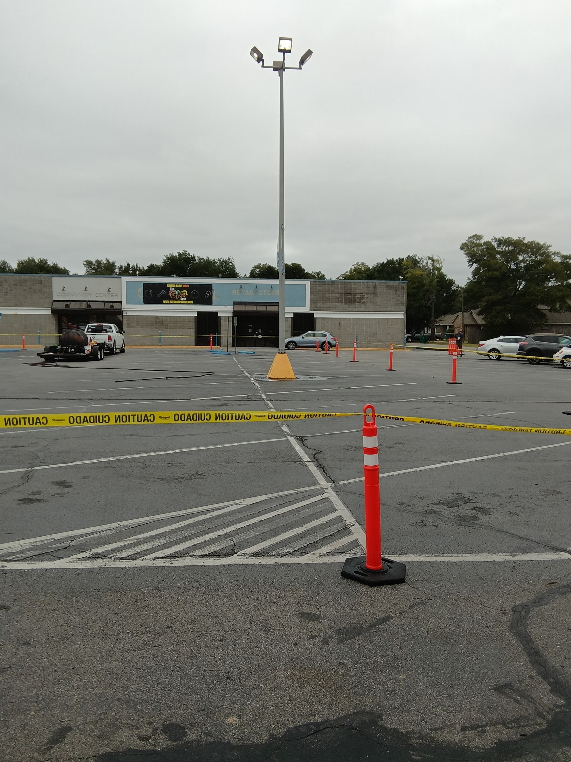 Exterior of building and parking lot with caution tape, orange traffic posts, and damaged entrance.
