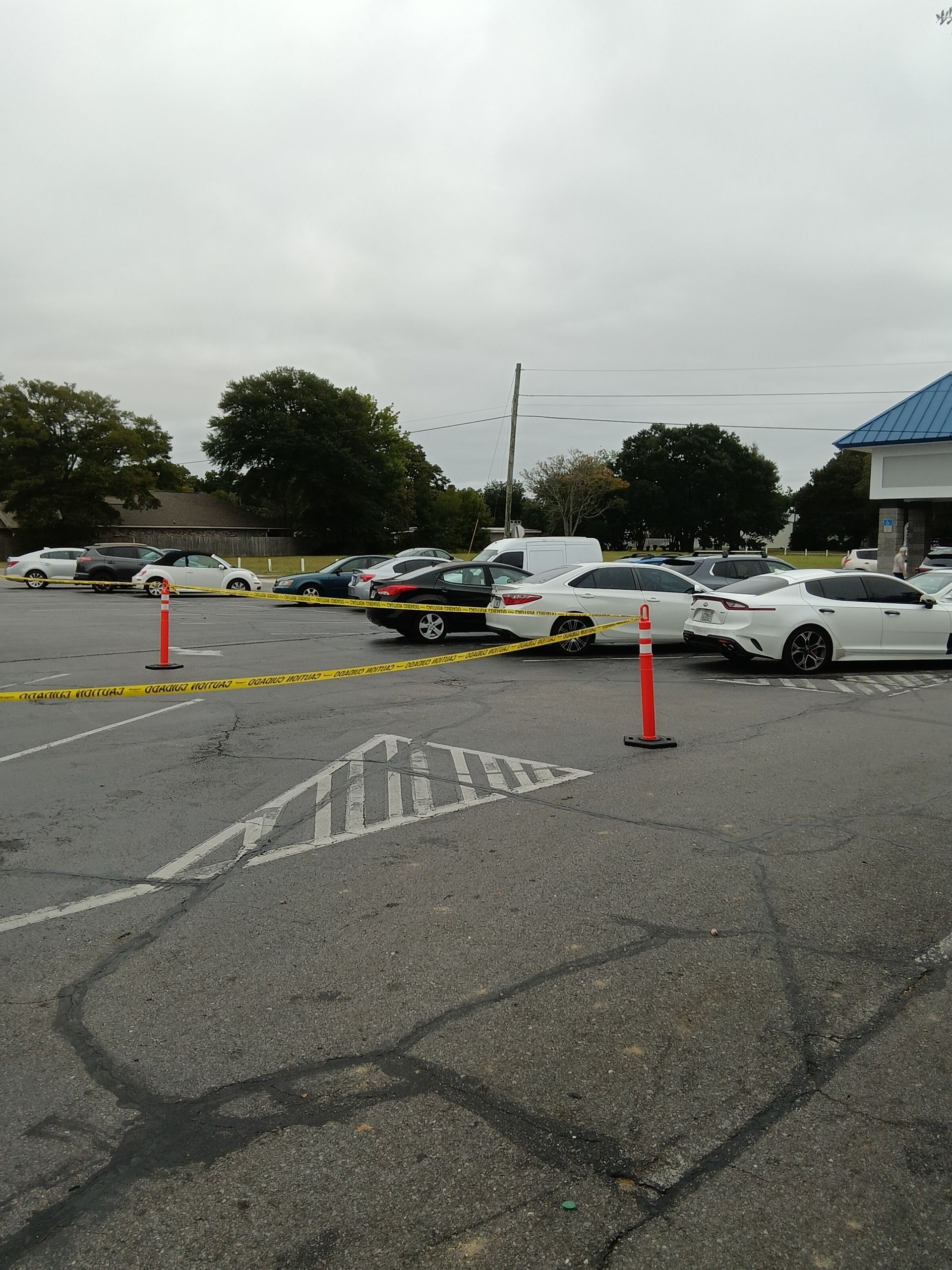 Parking lot with cars, yellow tape, and a building on an overcast day.