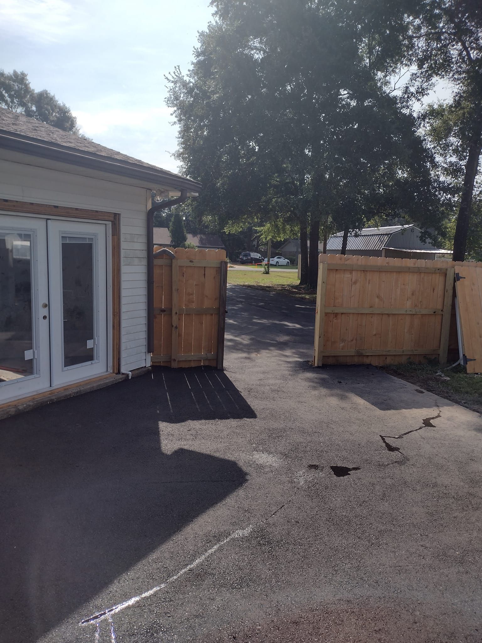 Asphalt driveway with wooden gate, open, leading to street.
