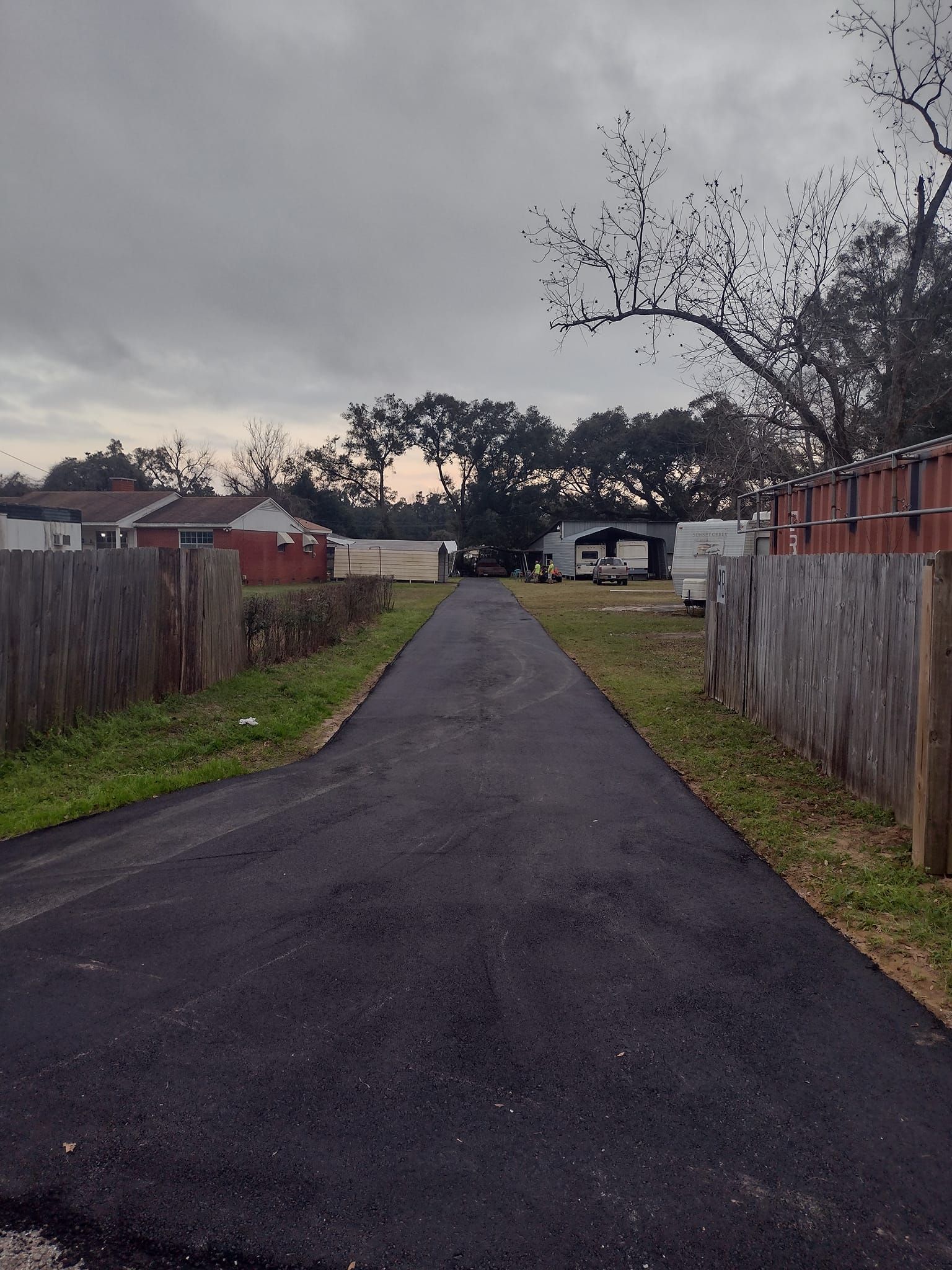 Paved alleyway between wooden fences, leading to a cloudy sky and distant buildings.