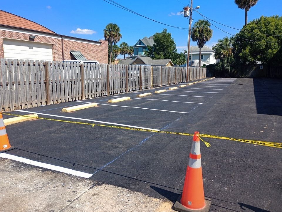 Empty asphalt parking lot with white lines, wooden fence, and orange traffic cones.